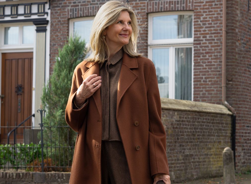 Damesmodel in een lange bruine jas met daaronder een bruine blouse en bijpassende broek.